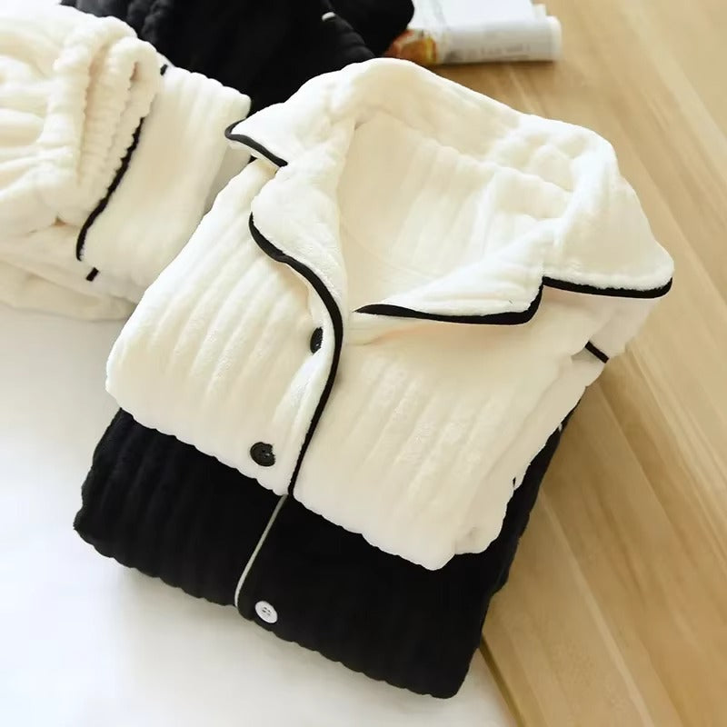 Pyjama femme chaud et confortable, plié soigneusement, avec haut crème à col revers et boutons noirs, bordures contrastantes noires, posé sur un bas noir. Ensemble doux en tissu côtelé parfait pour l’hiver.