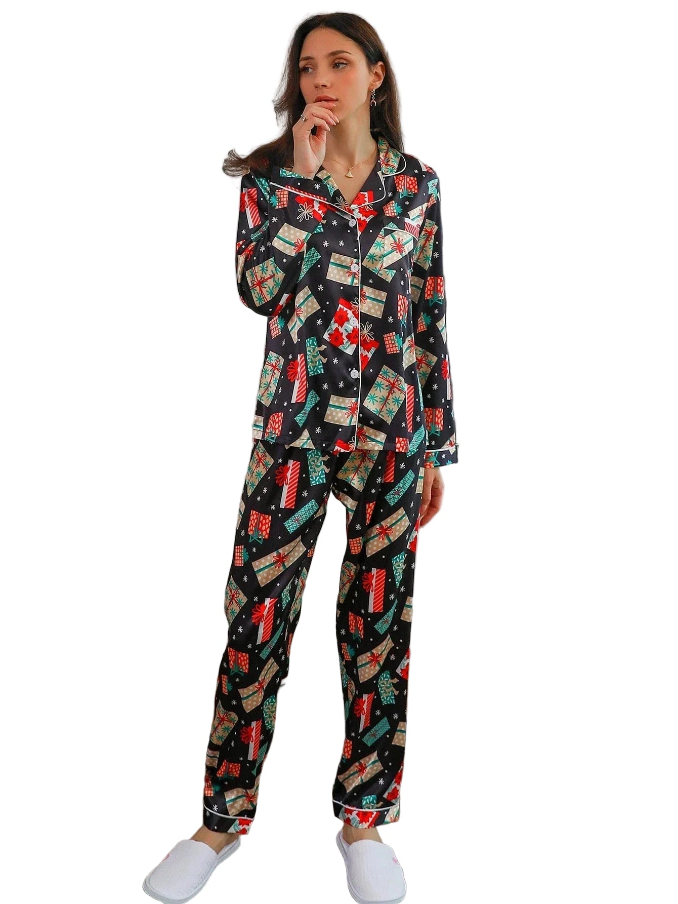 Femme portant le pyjama satin, un ensemble de Noël élégant et confortable en satin noir décoré de motifs festifs colorés  cadeaux, flocons et fleurs rouges comprenant une chemise à manches longues et un pantalon assorti, photographiée dans un intérieur moderne et lumineux.