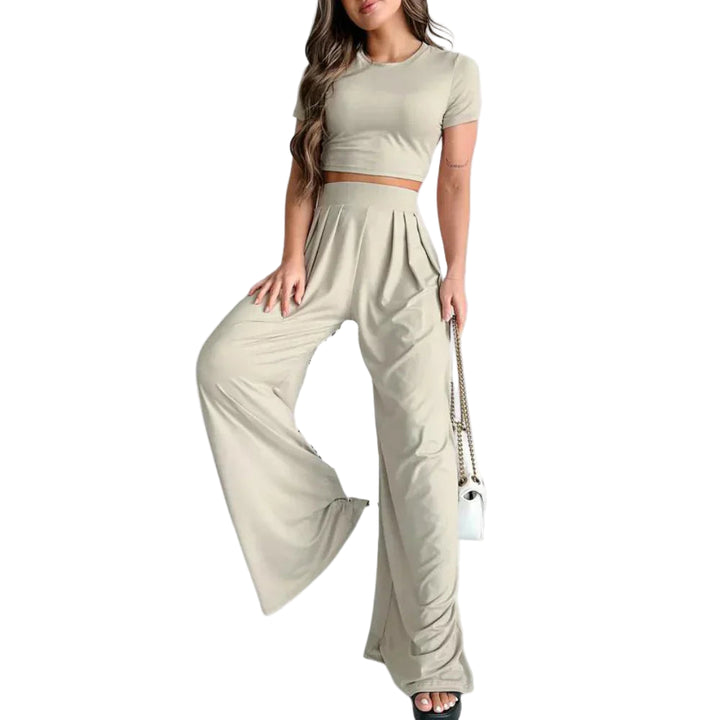 Femme portant l’ensemble Rosalind beige clair, composé d’un crop top à manches courtes et d’un pantalon taille haute large fluide. Tenue légère et confortable, parfaite pour l’été, les journées décontractées ou un look chic et décontracté.