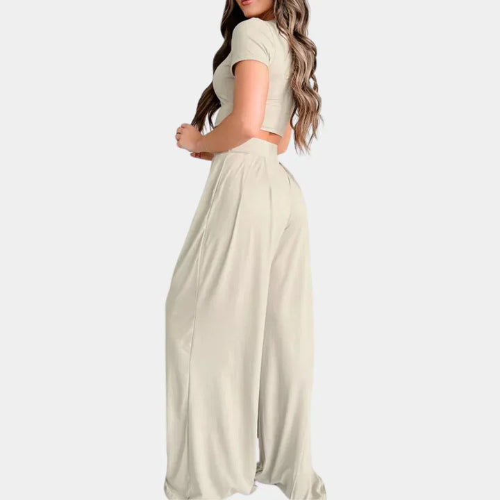 Femme portant l’ensemble Rosalind beige clair, composé d’un crop top à manches courtes et d’un pantalon taille haute large fluide. Tenue légère et confortable, parfaite pour l’été, les journées décontractées ou un look chic et décontracté.