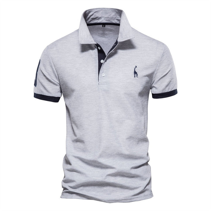 Polo pour homme de couleur grise avec des accents bleu marine sur le col et les manches. Il présente un logo de girafe bleu sur la poitrine. Ce polo allie confort et style, idéal pour une tenue décontractée et chic durant l&