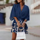 Femme portant une robe mini fleurie bleu marine avec un motif de feuilles dorées. Robe légère, confortable et idéale pour l'été, parfaite pour un look élégant et décontracté.