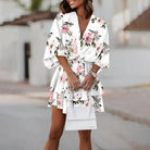 Femme portant une robe mini fleurie blanche avec des fleurs roses. Robe légère, confortable et idéale pour l’été, parfaite pour un look frais et élégant.
