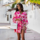 Femme portant une robe mini fleurie rose avec des motifs floraux colorés, légère et confortable. Idéale pour l'été, parfaite pour une journée décontractée tout en restant élégante.