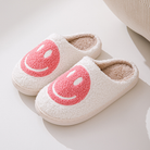 Chaussons unisexe Sasha blancs en matière pelucheuse avec grand motif smiley rose, doublure intérieure chaude et moelleuse, semelle confortable, idéals pour un confort cosy à la maison.