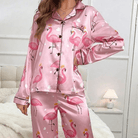 Femme portant un pyjama en satin rose à motifs flamants roses avec couronnes et petits cœurs blancs, composé d’un haut boutonné à col à revers et d’un pantalon long assorti. Pyjama tendance, ludique et confortable, parfait pour des nuits douces avec style.