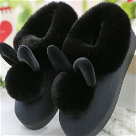 Chaussons d’intérieur noirs doublés de fausse fourrure, avec gros pompons et petites oreilles décoratives, pour garder les pieds bien au chaud à la maison.