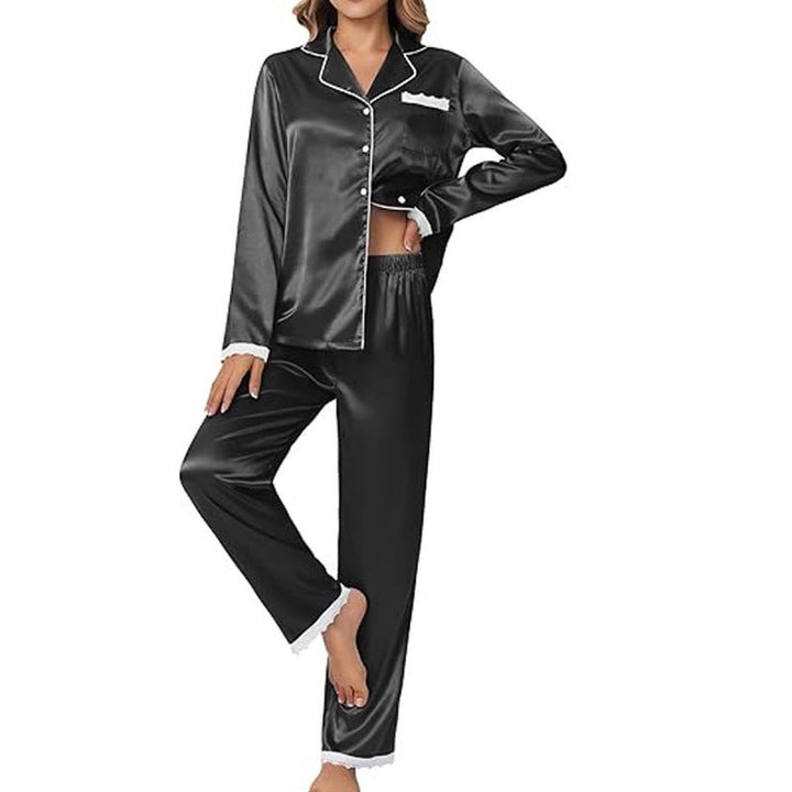 Femme portant un pyjama en satin noir, élégant et confortable, avec des détails en dentelle blanche aux poignets et aux chevilles. Le haut à manches longues est boutonné, tandis que le pantalon a une coupe droite et fluide. Elle pose avec une main sur la hanche, mettant en valeur la coupe soignée et le style raffiné du pyjama