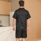 Vue de dos d’un homme portant le shorty en satin pour homme Sylvain, ensemble noir satiné à motifs discrets avec chemise à manches courtes et short assorti, coupe fluide et confortable mettant en valeur la légèreté du tissu, idéal pour des moments de détente élégants à la maison ou pour la nuit.