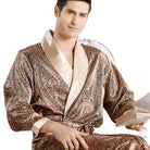 Homme portant le peignoir Tanguy, un modèle tendance et agréable en satin doré à motifs, assis et tenant un livre sur fond blanc.