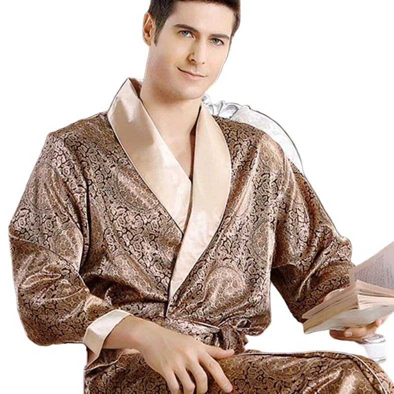 Homme portant le peignoir Tanguy, un modèle tendance et agréable en satin doré à motifs, assis et tenant un livre sur fond blanc.