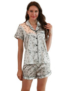 Femme portant le pyjama femme, un ensemble léger et élégant en satin blanc imprimé de motifs floraux discrets, composé d’une chemise à manches courtes et d’un short assorti.