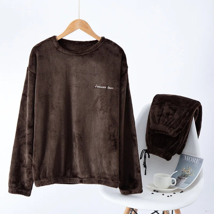 Pyjama femme Valérie en polaire marron chocolat, avec un haut à manches longues suspendu sur cintre et un pantalon assorti posé sur une chaise blanche. Ensemble chaud, doux et confortable, idéal pour les soirées cocooning en hiver.