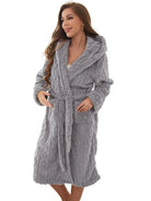 Peignoir femme Vanessa gris clair, doux et confortable, texture torsadée avec capuche, ceinture à nouer et poches, porté debout dans une chambre lumineuse.