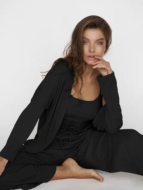 Femme assise portant un ensemble nuisette noir, composé d'un top sans manches et d'un pantalon fluide à taille élastiquée. Elle porte également une veste légère assortie, créant un look à la fois élégant et décontracté. Elle pose avec une expression naturelle et confiante, mettant en valeur le confort et le style raffiné de cet ensemble.