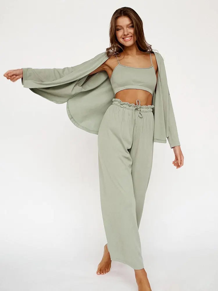 Femme souriante portant un ensemble nuisette vert pastel, composé d'un top sans manches et d'un pantalon fluide à taille élastiquée. Elle porte également une veste légère assortie, créant un look décontracté et élégant. Elle pose joyeusement, mettant en valeur le confort et la simplicité de cet ensemble chic.