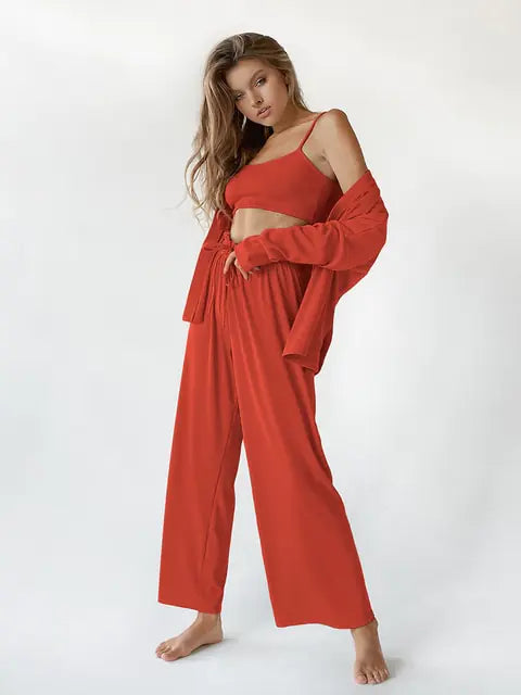 Femme souriante portant un ensemble nuisette rouge, composé d'un top sans manches et d'un pantalon fluide à taille élastiquée. Elle porte également une veste légère assortie, créant un look à la fois chic et décontracté. Elle pose avec confiance, mettant en valeur le confort et l'élégance de cet ensemble.