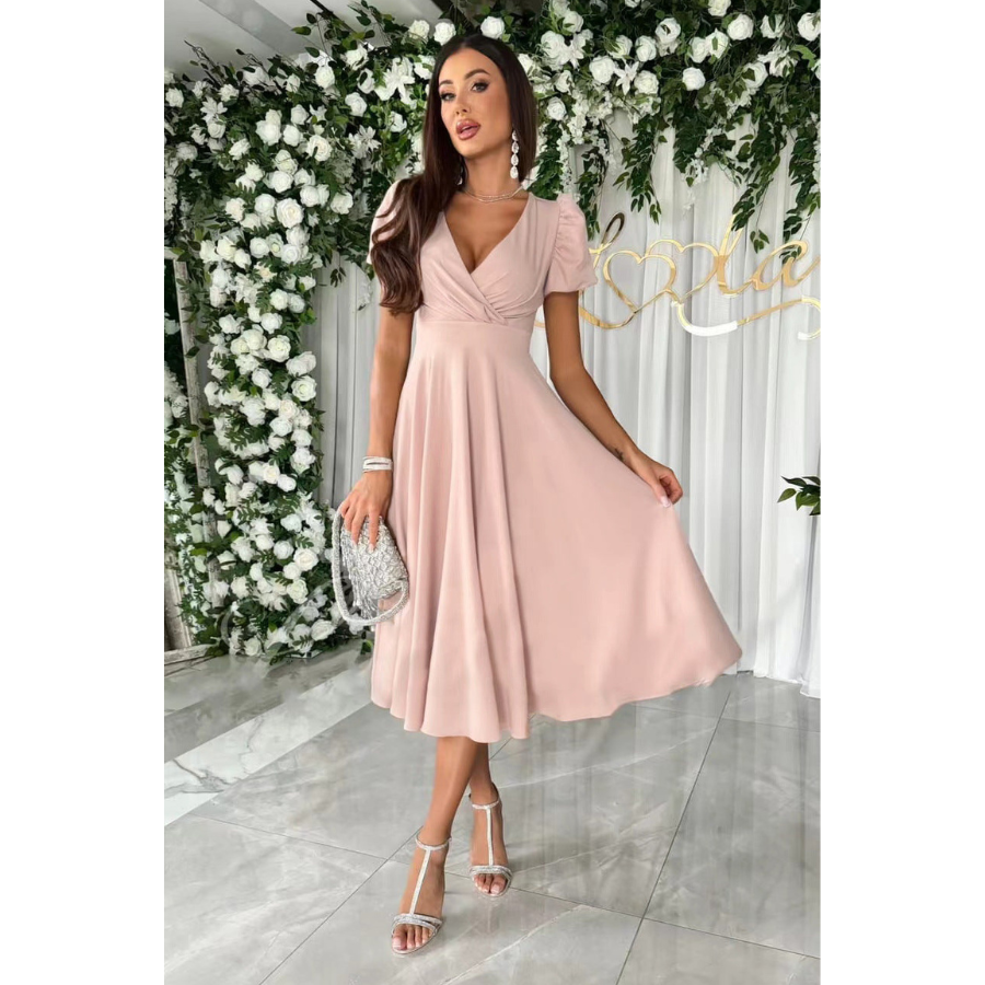 Élégante et fluide. Cette robe rose pâle à la coupe évasée et au décolleté en V, avec des manches bouffantes, crée une silhouette féminine et raffinée. Accessoirisée avec un sac à main argenté, elle est parfaite pour des occasions spéciales.