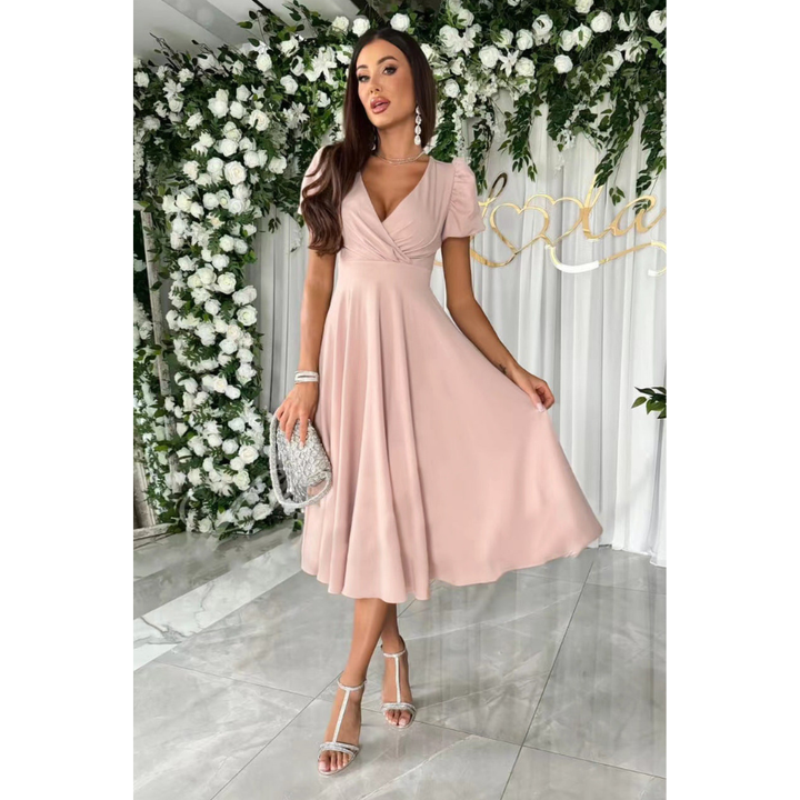 Élégante et fluide. Cette robe rose pâle à la coupe évasée et au décolleté en V, avec des manches bouffantes, crée une silhouette féminine et raffinée. Accessoirisée avec un sac à main argenté, elle est parfaite pour des occasions spéciales.