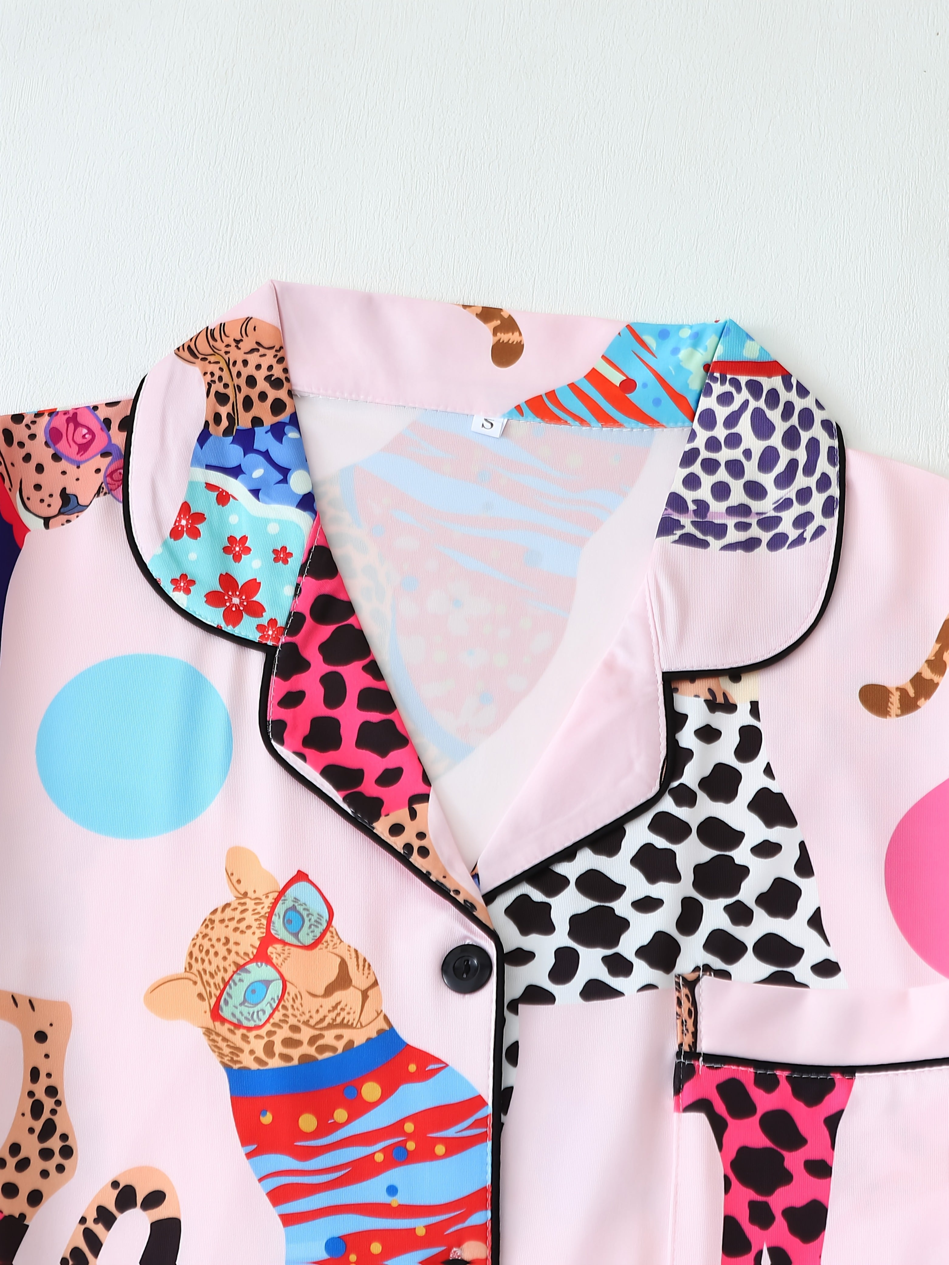 Gros plan sur le col et la poche poitrine du pyjama femme Verity, en satin rose à imprimés léopard colorés et détails contrastants noirs. Design fun et moderne avec finitions soignées, parfait pour une tenue de nuit à la fois stylée et confortable.