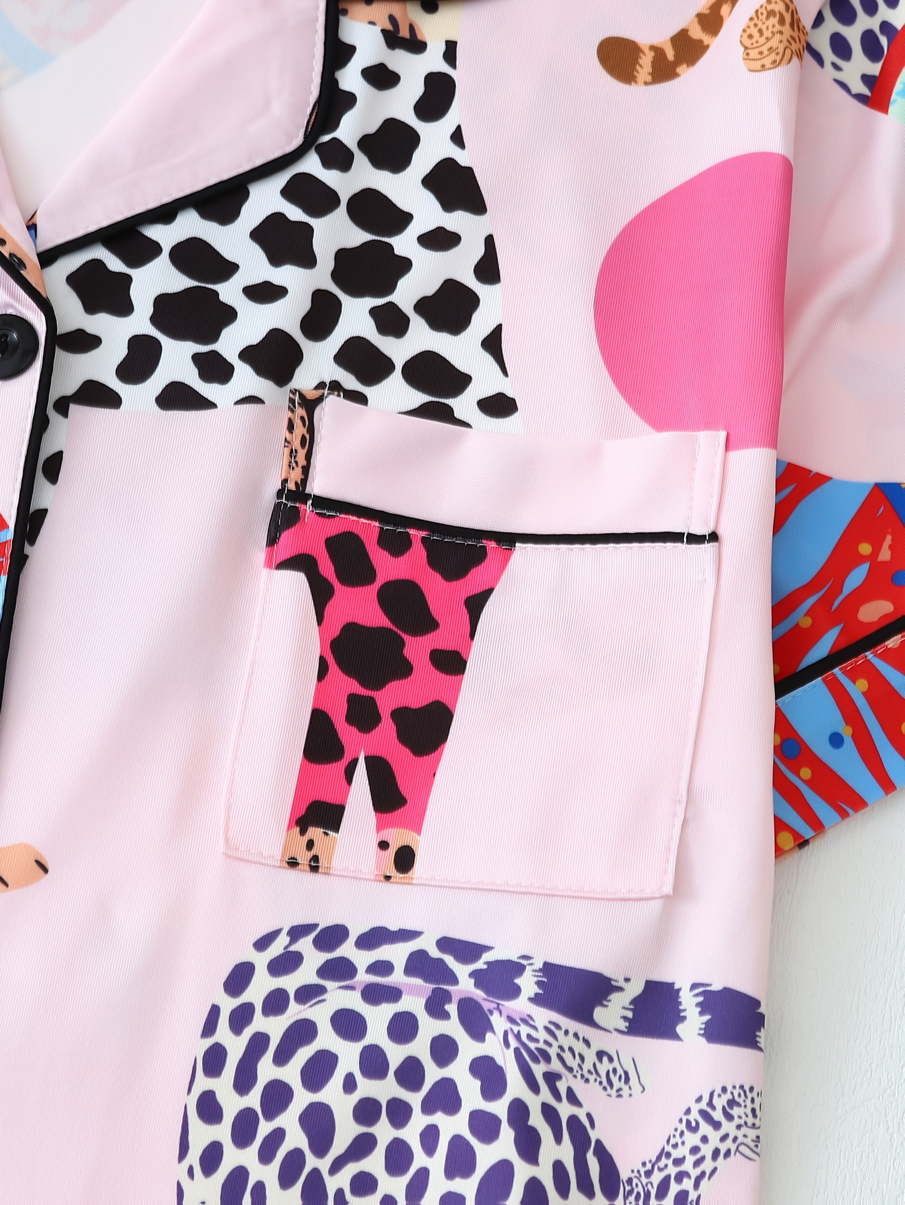 Zoom sur la poche poitrine du pyjama femme Verity, en satin rose décoré de motifs félins colorés et détails contrastants noirs. Design original et ludique, offrant une touche tendance tout en assurant confort et style pour la nuit.