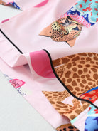 Détail du tissu et des finitions du pyjama Verity, montrant un ourlet soigné avec passepoil noir et imprimés félins multicolores sur satin rose. Matière douce, fluide et agréable au toucher, idéale pour un style original et relaxant à la maison.