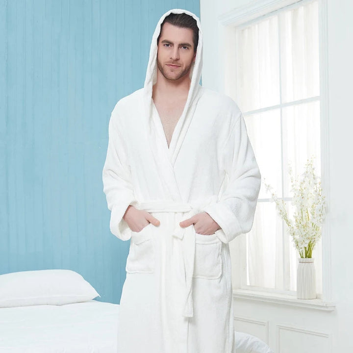 un peignoir blanc à capuche en tissu doux avec ceinture et poches avant, offrant chaleur, élégance et confort pour la détente à la maison.