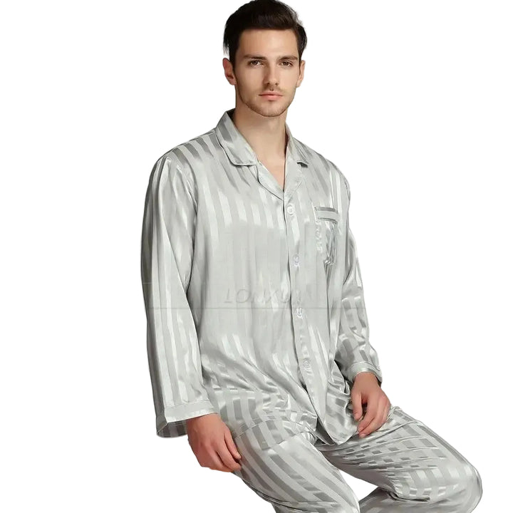 Homme portant le pyjama, un ensemble élégant en satin gris brillant à rayures ton sur ton, composé d’une chemise à boutons et d’un pantalon assorti. Pyjama doux, confortable et raffiné, idéal pour la nuit.