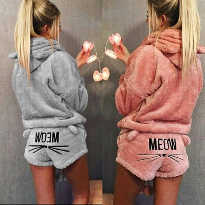 Deux versions du pyjama Whitaker pour femme, un ensemble doux et chaud en matière pelucheuse avec capuche à oreilles de chat et short assorti décoré du mot « MEOW » et de moustaches, présentées en gris et en rose pour un style à la fois confortable et amusant.