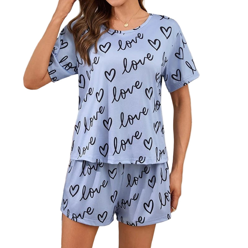 Femme portant un pyjama court bleu clair à manches courtes, décoré de motifs "love" et de cœurs noirs. Ensemble composé d’un t-shirt ample et d’un short assorti. Tenue douce, légère et confortable, idéale pour les nuits d’été ou les moments de détente à la maison.