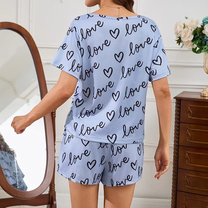 Vue arrière d’une femme portant un pyjama court bleu clair à imprimé "love" et cœurs noirs. Ensemble composé d’un t-shirt à manches courtes et d’un short assorti. Tenue confortable, douce et tendance, parfaite pour l’été ou les soirées détente à la maison.
