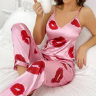 Pyjama satin femme Zéphyrine rose avec imprimé lèvres rouges, ensemble tendance et agréable avec caraco à fines bretelles et pantalon long satiné, porté assise sur un lit, tissu brillant et doux.