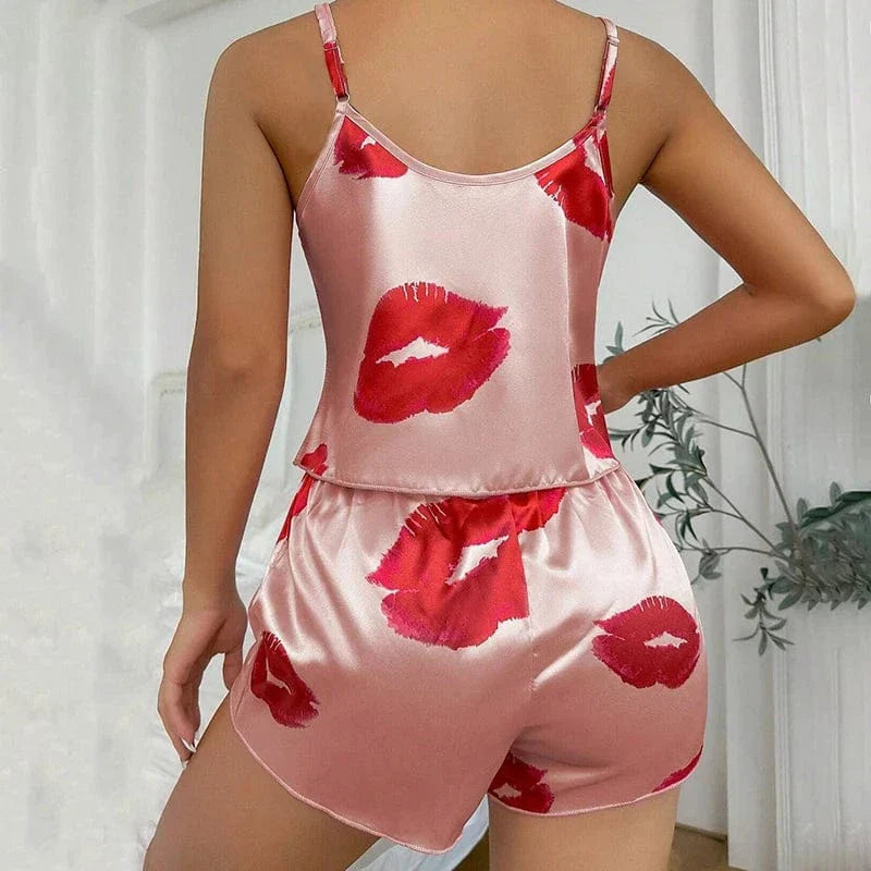 Vue arrière d’une femme portant un ensemble shorty en satin rose clair orné de baisers rouges. Haut à fines bretelles et dos droit, avec short assorti à taille élastique. Ensemble tendance, féminin et agréable à porter, parfait pour les soirées cocooning ou les nuits estivales.