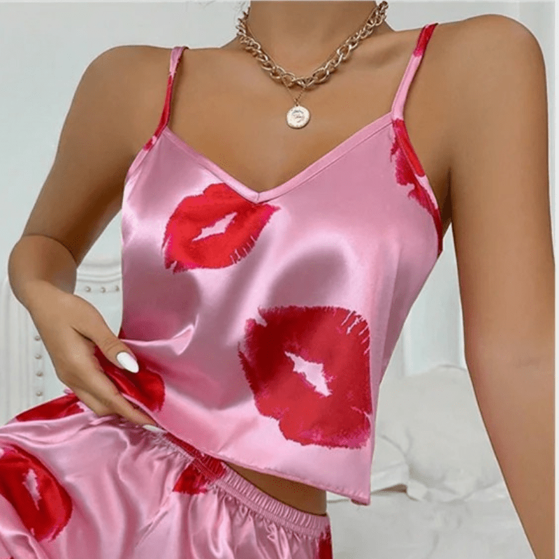 Gros plan sur un ensemble shorty satiné rose orné de baisers rouges. Le haut à fines bretelles possède une encolure en V, et le short assorti présente une taille élastique. Tenue féminine, tendance et agréable à porter, idéale pour les nuits estivales ou les instants cocooning.