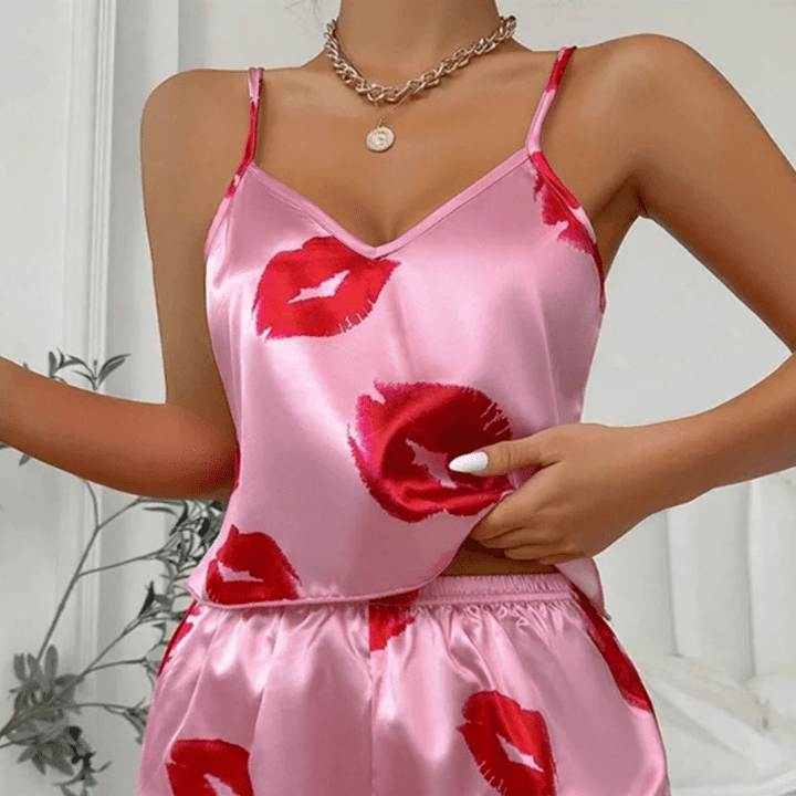 Gros plan sur un ensemble shorty en satin rose vif avec imprimé de baisers rouges. Haut à fines bretelles et encolure en V, associé à un short fluide à taille élastique. Tenue tendance, douce et agréable à porter, idéale pour les nuits d’été ou les moments de détente féminins et stylés.
