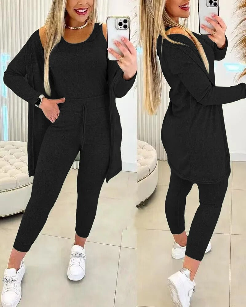 Femme vêtue de l’ensemble Axelle en noir, composé d’un débardeur, d’un legging taille haute à cordon et d’un long gilet assorti. Une tenue élégante et confortable, idéale pour se détendre avec style ou pour une sortie décontractée.