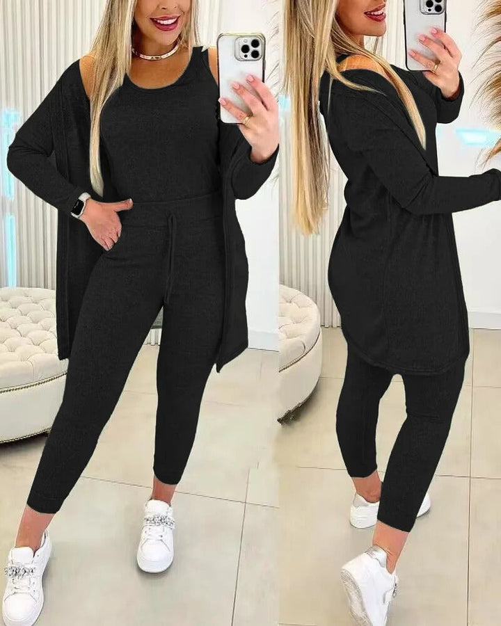 Femme vêtue de l’ensemble Axelle en noir, composé d’un débardeur, d’un legging taille haute à cordon et d’un long gilet assorti. Une tenue élégante et confortable, idéale pour se détendre avec style ou pour une sortie décontractée.