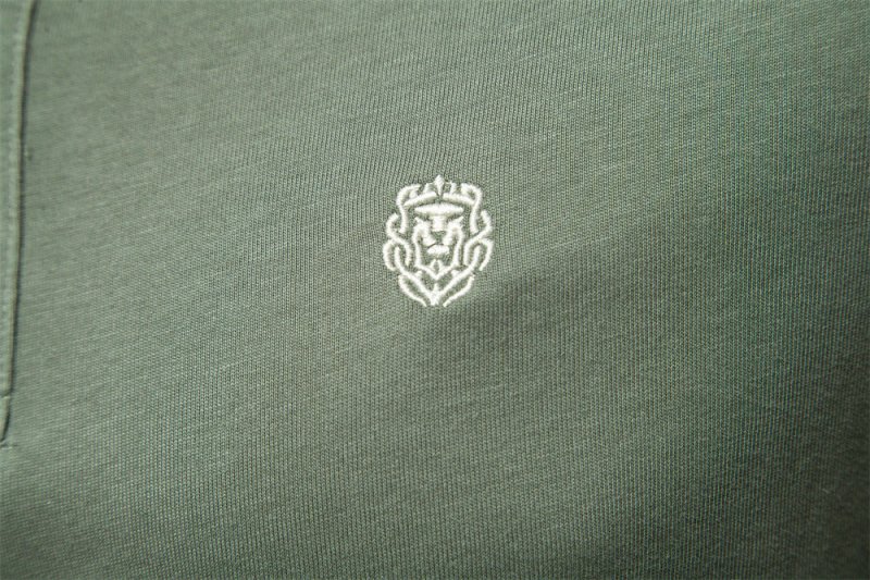 Détail du logo brodé sur la poitrine du polo vert kaki pour homme. Ce logo discret en fil blanc ajoute une touche de raffinement, tout en maintenant le style épuré et élégant du polo, idéal pour les journées estivales.