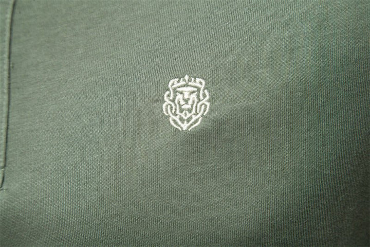 Détail du logo brodé sur la poitrine du polo vert kaki pour homme. Ce logo discret en fil blanc ajoute une touche de raffinement, tout en maintenant le style épuré et élégant du polo, idéal pour les journées estivales.