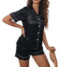 Femme portant le pyjama Élise, ensemble noir satiné à manches courtes et short assorti avec liserés blancs élégants. Tissu léger, doux au toucher et coupe raffinée pour un look chic et confortable à la maison.