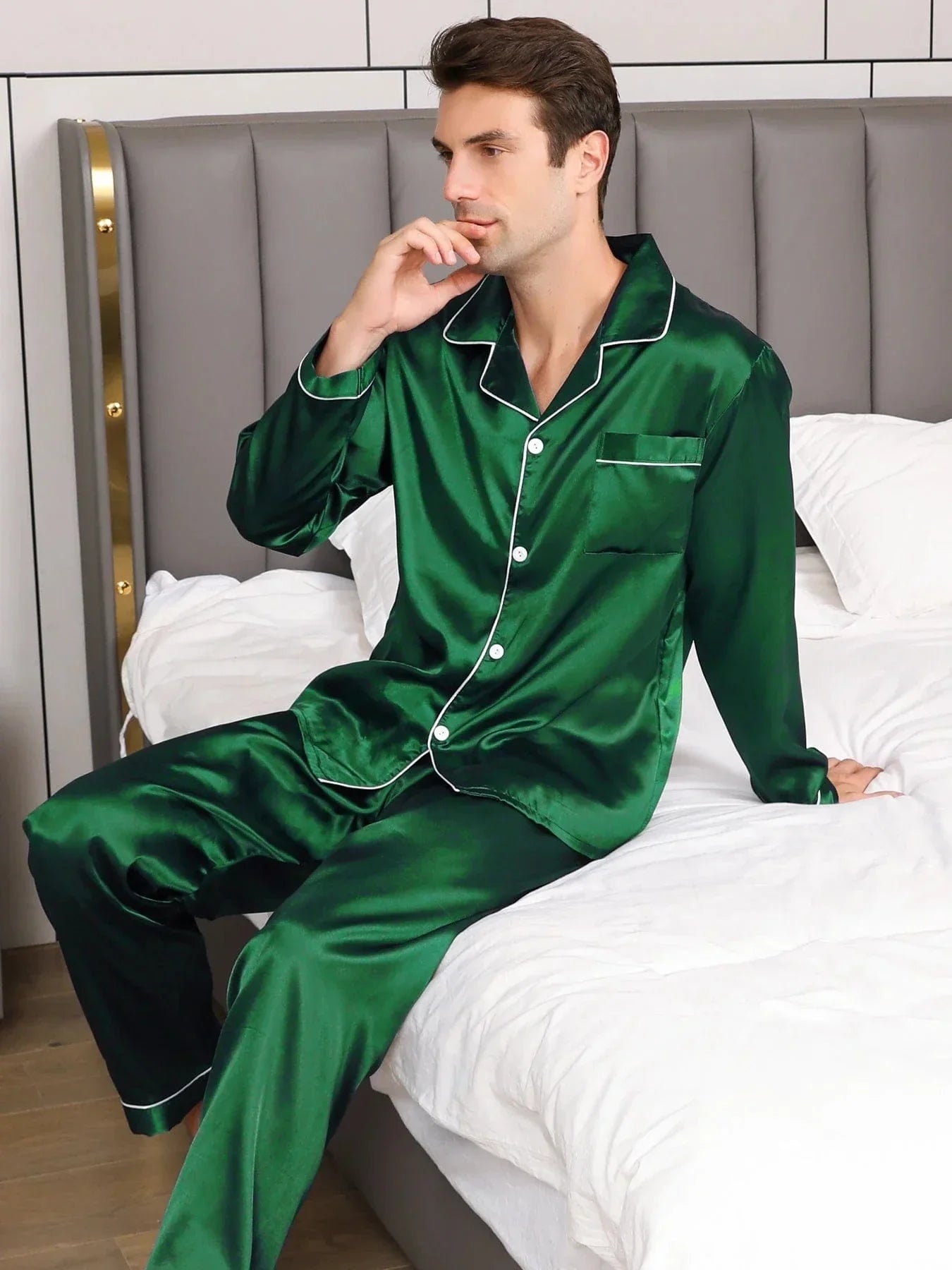 Pyjama en satin pour homme, de couleur vert émeraude, composé d'une chemise élégante avec une poche et un pantalon assorti. Le modèle est assis sur un lit, en train de réfléchir, arborant un look chic et détendu. Ce pyjama allie confort et raffinement, parfait pour des moments de relaxation à la maison avec une touche de sophistication.
